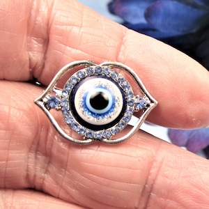 May include: A silver-toned evil eye charm with a blue and white eye design surrounded by clear blue rhinestones.