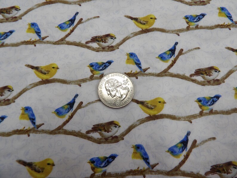 May include: Fabric with a repeating pattern of colorful birds perched on brown branches against a white background. The birds are yellow, blue, and brown. A U.S. quarter coin is included for scale.