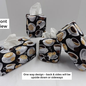 May include: Four tissue box covers with a coffee cup and cookie design. The covers are black with white coffee cups and brown cookies. The tissue boxes are on a white surface. "Front View" is written in black text on the left side of the image. "One way design - back & sides will be upside down or sideways" is written in black text at the bottom of the image.