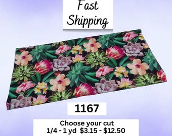 May include: A rectangular piece of fabric featuring a black background with a dense, colorful pattern of various succulents and hibiscus flowers in shades of green, pink, peach, and yellow. The fabric is labeled with the number 1167.