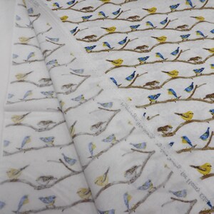 May include: White fabric with a repeating pattern of birds perched on brown branches. The birds are depicted in yellow, blue, and brown hues. The fabric is folded, showing the pattern's continuity.