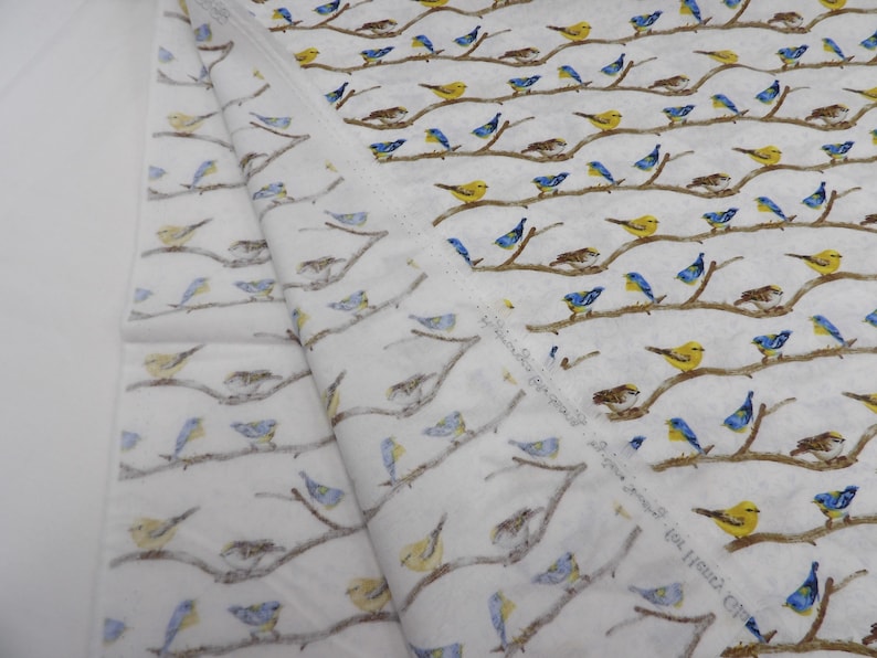 May include: White fabric with a repeating pattern of birds perched on brown branches. The birds are depicted in yellow, blue, and brown hues. The fabric is folded, showing the pattern's continuity.