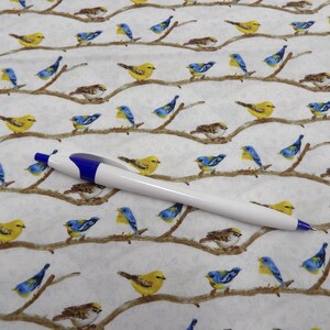 May include: White and blue ballpoint pen on a white fabric patterned with yellow, blue, and brown birds perched on branches. The birds are in various poses, creating a nature-themed design.