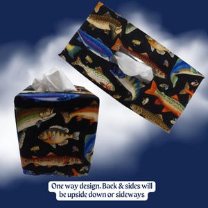 May include: Two rectangular tissue box covers featuring a black fabric base with a colorful pattern of various fish and fishing lures. White tissues protrude from the top openings. Text on the image reads: One way design. Back & sides will be upside down or sideways.