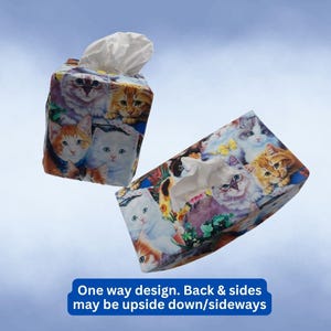May include: Two rectangular tissue box covers featuring a colorful print of various cat faces. The boxes are decorated with illustrations of white, orange, and grey cats. Text on the image states: One way design. Back & sides may be upside down/sideways.