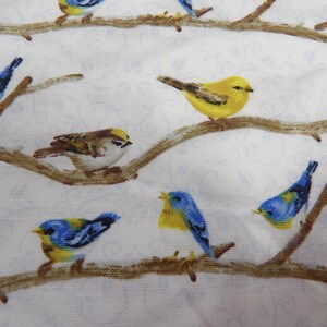 May include: A white fabric with a repeating pattern of birds perched on brown branches. The birds are various colors, including yellow, blue, and brown. The background has a subtle floral design.
