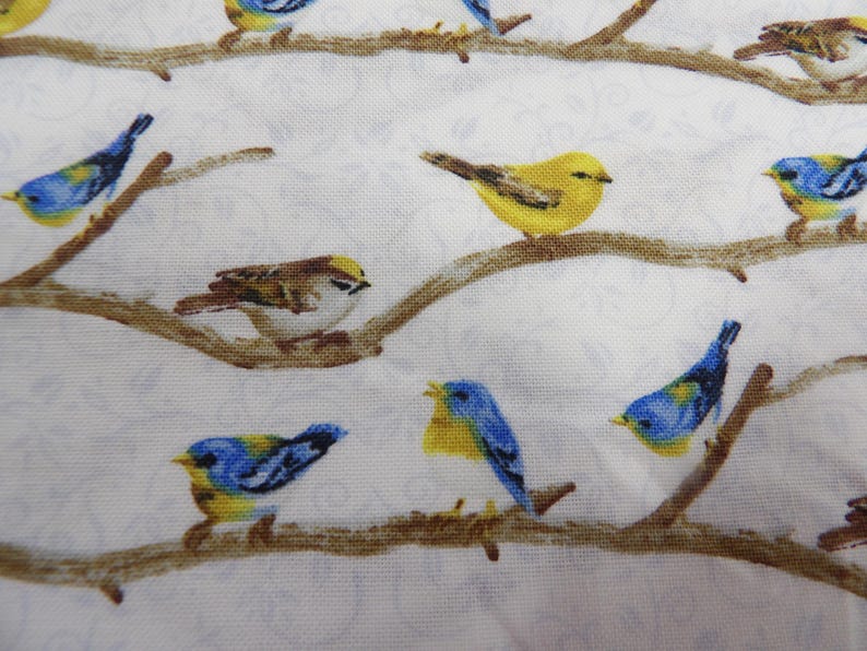 May include: A white fabric with a repeating pattern of birds perched on brown branches. The birds are various colors, including yellow, blue, and brown. The background has a subtle floral design.