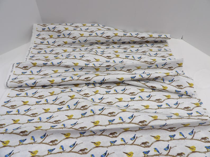 May include: White fabric with a repeating pattern of birds perched on brown branches. The birds are depicted in yellow and blue, with some nests visible. The fabric is folded, showing the pattern's continuity. Ideal for crafting or home decor projects.