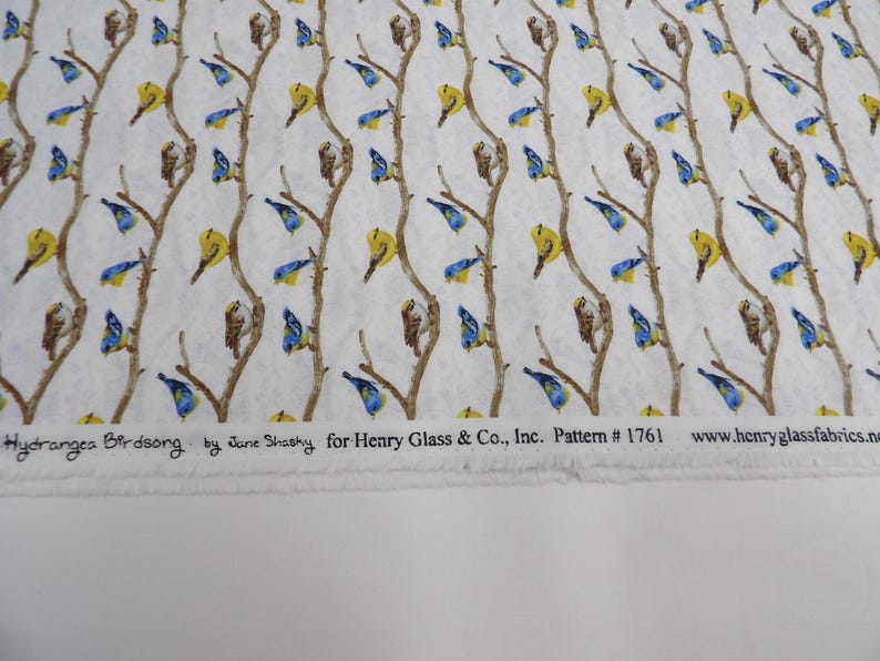 May include: White fabric with a repeating pattern of brown branches, yellow and blue birds. The text "Hydrangea Birdsong" and other details are printed along the bottom edge. Pattern #1761.