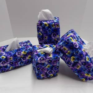 May include: Four tissue box covers with a floral pattern of purple and yellow pansies on a blue background.