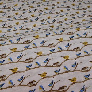 May include: White fabric with a repeating pattern of birds perched on brown branches. The birds are depicted in yellow, blue, and brown, creating a nature-inspired design. The branches are arranged in a diagonal pattern.
