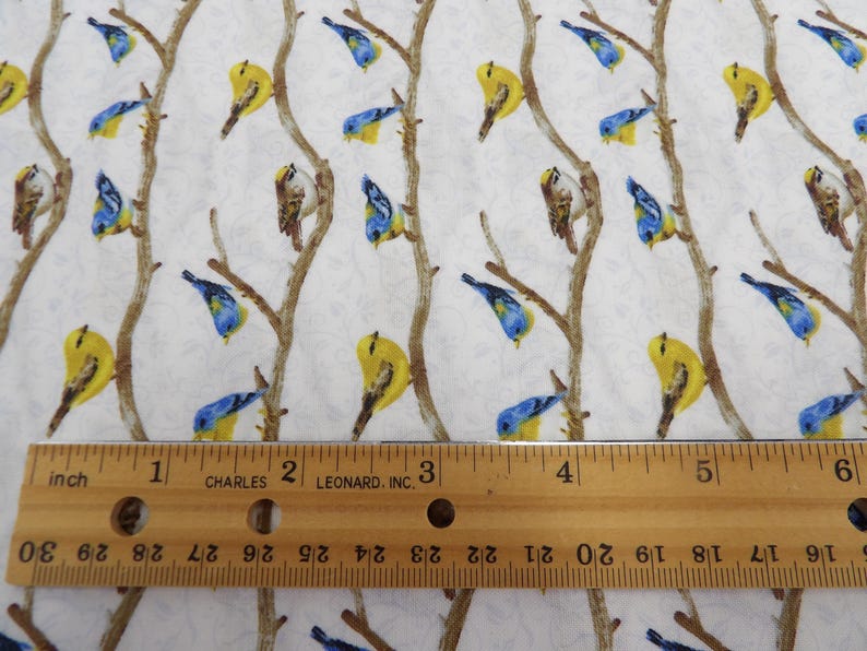 May include: White fabric with a repeating pattern of birds perched on brown branches. The birds are yellow, blue, and brown. A wooden ruler with inch measurements is in the foreground.