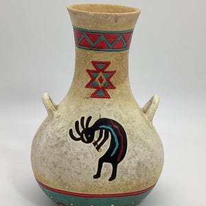 May include: A ceramic vase with a beige background and Native American-inspired designs. The vase features a red, blue, and yellow geometric pattern, a black and blue stylized figure, and a red, green, and white border.