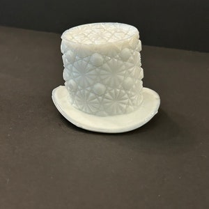 May include: A white milk glass hat with a diamond pattern. The hat has a wide brim and a tall crown.
