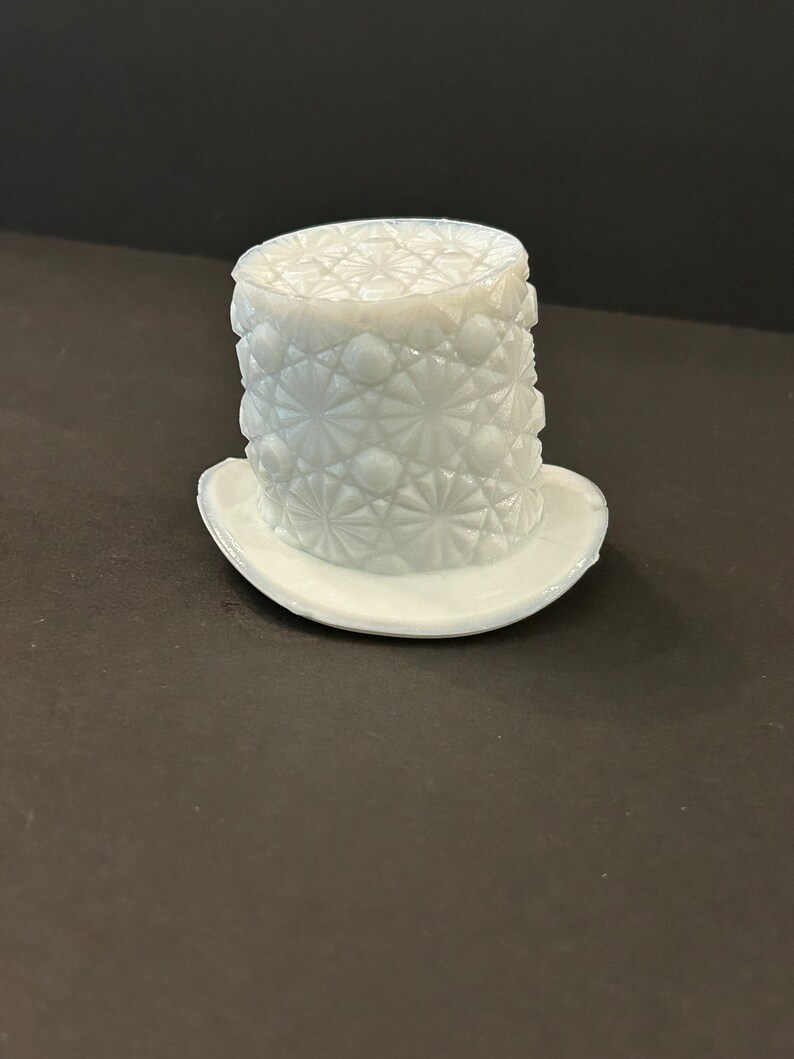 May include: A white milk glass hat with a diamond pattern. The hat has a wide brim and a tall crown.