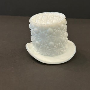 May include: A white glass hat with a diamond pattern. The hat is made of pressed glass and has a wide brim.