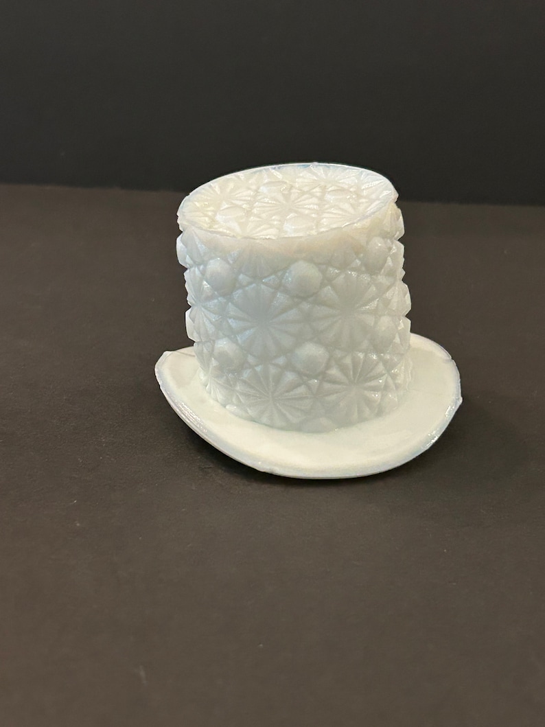 May include: A white glass hat with a diamond pattern. The hat is made of pressed glass and has a wide brim.