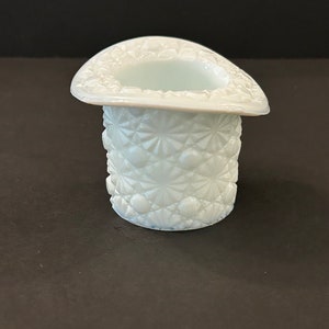 May include: A white milk glass hat shaped trinket dish with a raised, starburst pattern.