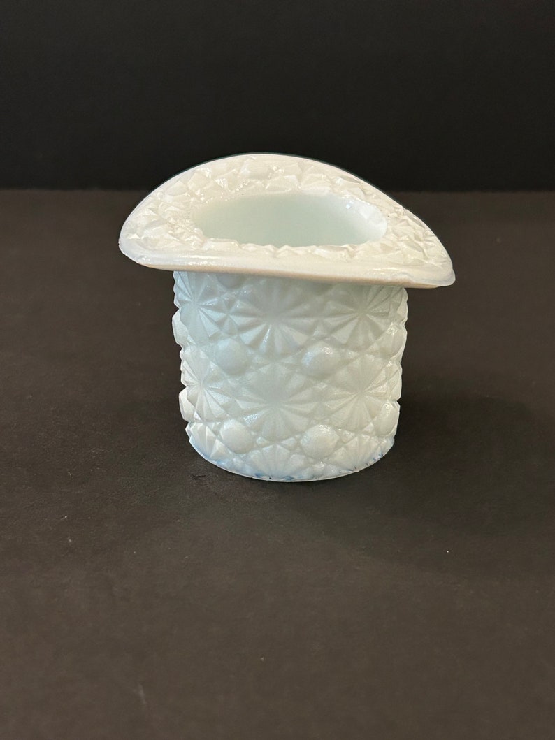 May include: A white milk glass hat shaped trinket dish with a raised, starburst pattern.