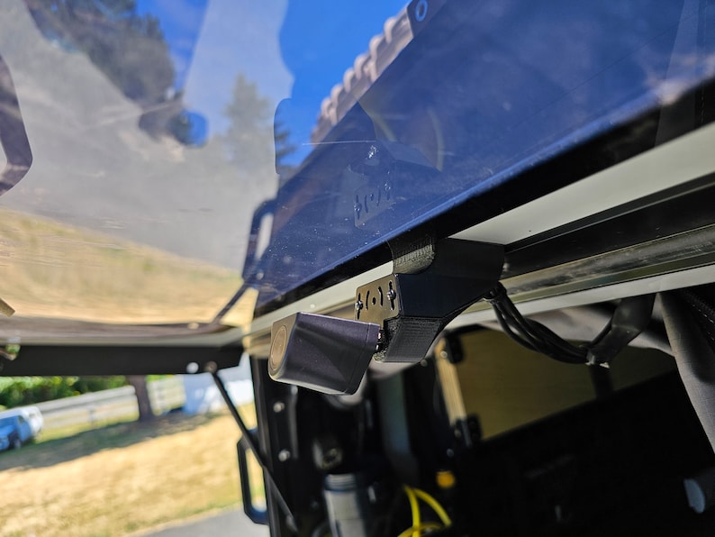 May include: A black rear-view camera mounted on a vehicle with black wiring.