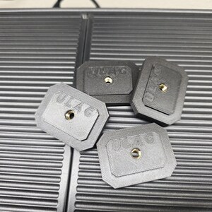May include: Four small, rectangular, gray and black objects with the text "ULAG" and a central hole. The objects are arranged on a textured, dark gray surface.