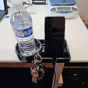 May include: A black plastic car organizer with a cup holder, a phone holder, and a key hook. A clear plastic water bottle is in the cup holder. A black smartphone is in the phone holder.