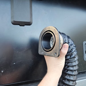 Könnte beinhalten: Ein schwarzer flexibler Schlauch mit einem Metallanschluss, der an einem silbernen und schwarzen Metallentlüftungsrohr befestigt ist.