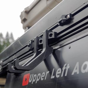 May include: Black plastic hooks mounted on a black metal track with the text "Upper Left Adve" visible on the side.