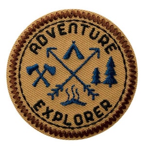 May include: A brown and tan embroidered patch with the words "Adventure Explorer" in black. The patch features a blue tent, crossed arrows, and trees.