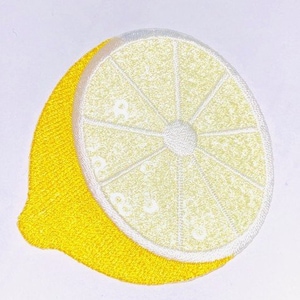 Pode incluir: Um remendo de limão bordado amarelo e branco. O limão está cortado ao meio e mostra o interior da fruta.