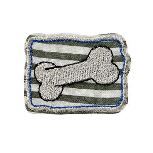 Könnte beinhalten: Ein grauer und weiß gestreifter Stoff-Patch mit einem silbernen gestickten Knochen in der Mitte. Der Patch hat einen blauen und silbernen gestickten Rand.