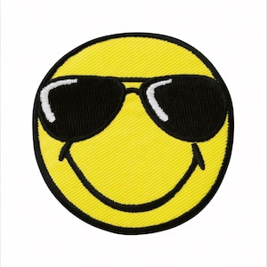 Könnte beinhalten: Gestickter gelber Smiley-Aufnäher mit schwarzer Sonnenbrille. Der Aufnäher hat einen schwarzen Rand und einen lächelnden Mund. Die Sonnenbrille hat weiße Highlights. Der Aufnäher ist rund und hat ein strukturiertes Aussehen.