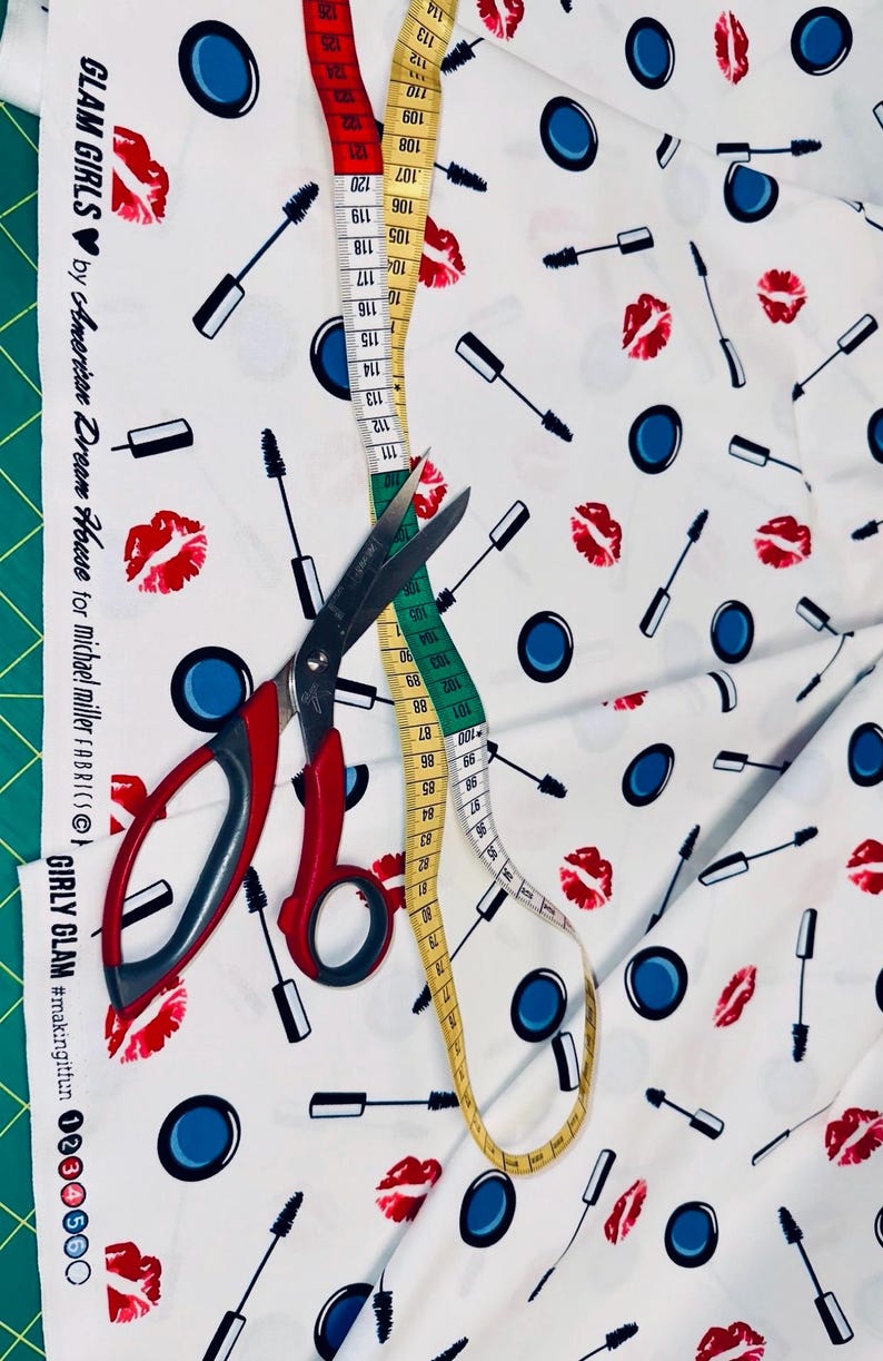 Baumwollstoff mit Kosmetik-Motiven, dekoriert mit Maßband und Stoffschere zur Größenorientierung.