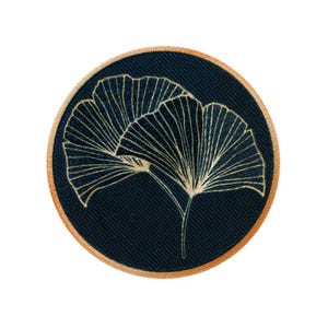 Könnte beinhalten: Ein runder, dunkelblauer Patch mit goldener Umrandung zeigt ein stilisiertes Bild von zwei Ginkgoblättern.