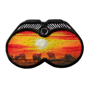 Pode incluir: Etiqueta bordada que representa uma cena de pôr do sol vista através de binóculos. A cena apresenta um pôr do sol laranja e amarelo brilhante com um sol branco e uma silhueta escura de árvores em primeiro plano.