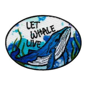 Könnte beinhalten: Gestickter Aufnäher mit einem blauen Wal, der aus dem Wasser springt, umgeben von grünem Seetang. Der Text "Let Whale Live" ist in schwarzem Garn auf weißem Hintergrund gestickt.
