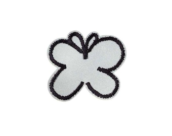 Op de afbeelding: Een vlindervormige geborduurde patch met een lichtgrijs midden en een dikke, donkerzwarte gestikte rand die de vleugels en het centrale lichaam omlijnt. Het ontwerp is symmetrisch met afgeronde vleugelvormen en een strakke uitstraling.