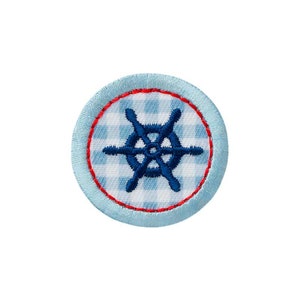 Könnte beinhalten: Ein blauer und weißer Gingham-Stoffkreis mit rotem Rand und einem blauen, gestickten nautischen Rad in der Mitte.