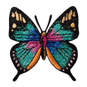 Könnte beinhalten: Ein bunter gestickter Schmetterlings-Patch mit türkisfarbenen, blauen, rosa, orangefarbenen und goldenen Akzenten. Der Schmetterling hat schwarze Umrisse und eine glitzernde Oberfläche.