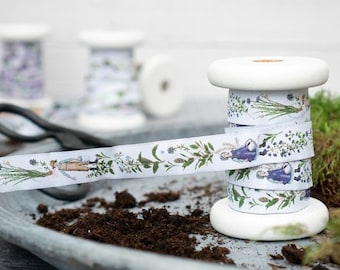 Pode incluir: Um carretel de fita branca com uma estampa floral e botânica com pequenas figuras. A fita está enrolada em torno de um carretel de madeira branco.