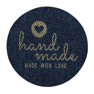 Könnte beinhalten: Ein rundes, blaues Jeans-Etikett mit goldener Stickerei, auf dem "handgefertigt" und "mit Liebe gemacht" steht. In der Mitte des Etiketts befindet sich ein kleines Herz.