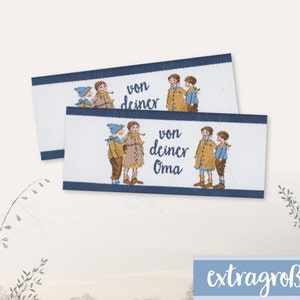 Könnte beinhalten: Zwei weiße Stoff-Etiketten mit blauem Rand und einem Cartoon-Bild von Kindern. Das obere Etikett lautet "von deiner" und das untere Etikett lautet "von deiner Oma".