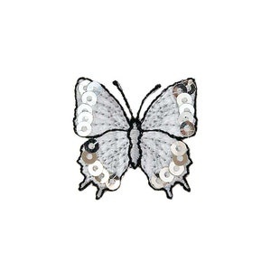 Op de afbeelding: Een witte geborduurde vlinder met zilveren pailletten. De vlinder heeft zwarte contouren en is een decoratieve patch.