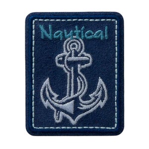 Könnte beinhalten: Ein blauer Stoff-Patch mit weißen Nähten an den Rändern. Der Patch zeigt einen weißen gestickten Anker mit dem Wort "Nautical" in blauer Stickerei darüber.