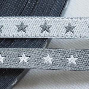 Könnte beinhalten: Zwei Rollen graues und weißes Band mit silbernen Sternen darauf gedruckt. Das Band ist in der Mitte gefaltet und die Enden sind sichtbar.