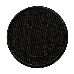 Könnte beinhalten: Schwarzer gestickter Smiley-Patch. Der Patch ist rund und hat einen schwarzen Hintergrund mit einem weißen Umriss.