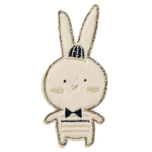 Könnte beinhalten: Ein weißer gestickter Hase mit einem marineblauen und weiß gestreiften Hemd, einer schwarzen Fliege und einem marineblauen Hut. Der Hase ist mit goldenen Glitzer umrandet.