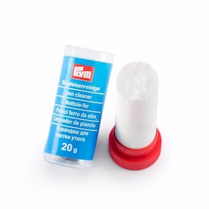 Könnte beinhalten: Ein Bügeleisenreiniger mit einem weißen, zylindrischen Reinigungsstab und einem roten Deckel. Das Produkt befindet sich in einem blau-weißen Behälter mit Text in mehreren Sprachen, darunter "Iron cleaner" und "20 g".