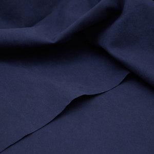 Könnte beinhalten: Nahaufnahme eines dunkelblauen Stoffes mit glatter Textur. Der Stoff ist in der Mitte gefaltet und erzeugt einen weichen, fließenden Effekt.