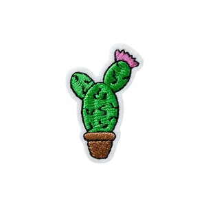 May include: A green cactus with a pink flower on top, potted in a brown pot. The cactus is embroidered on a white fabric.